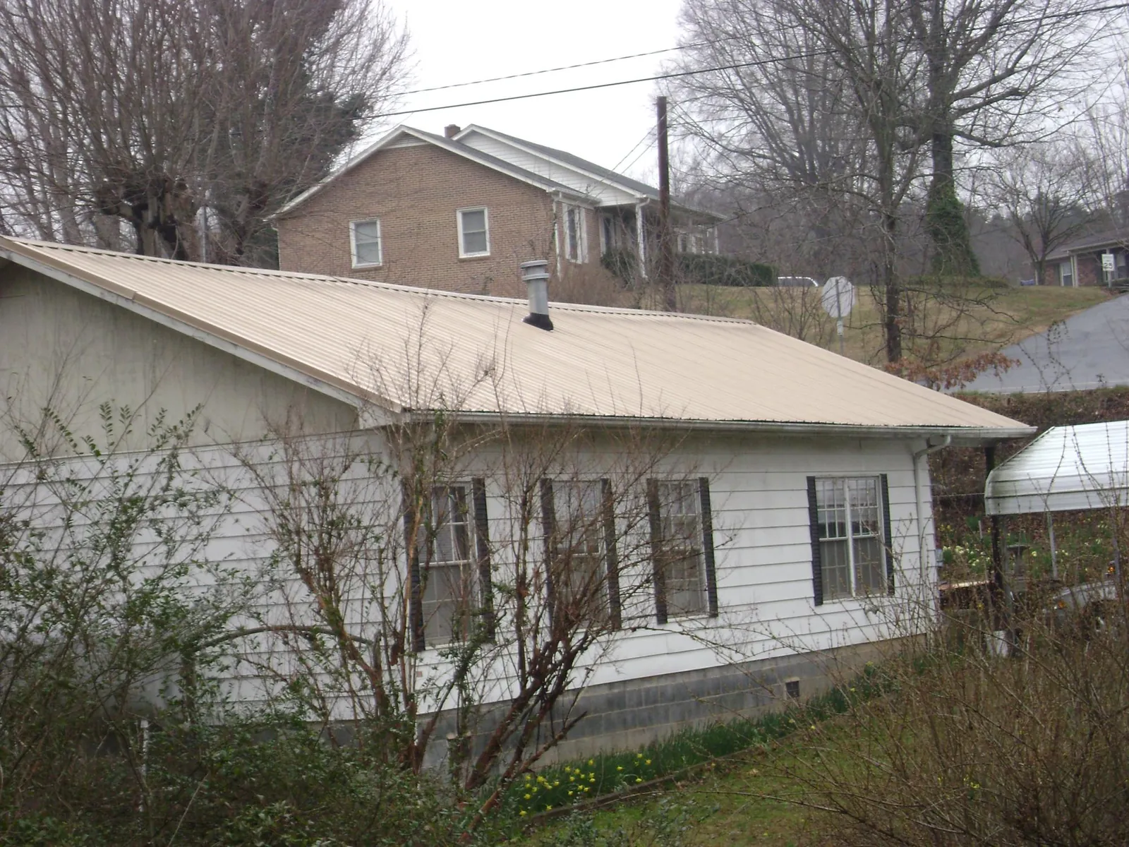 Tan metal roof on a white sided house set into a hillside — Commercial Roofing by Roofing Brothers in Saint George
